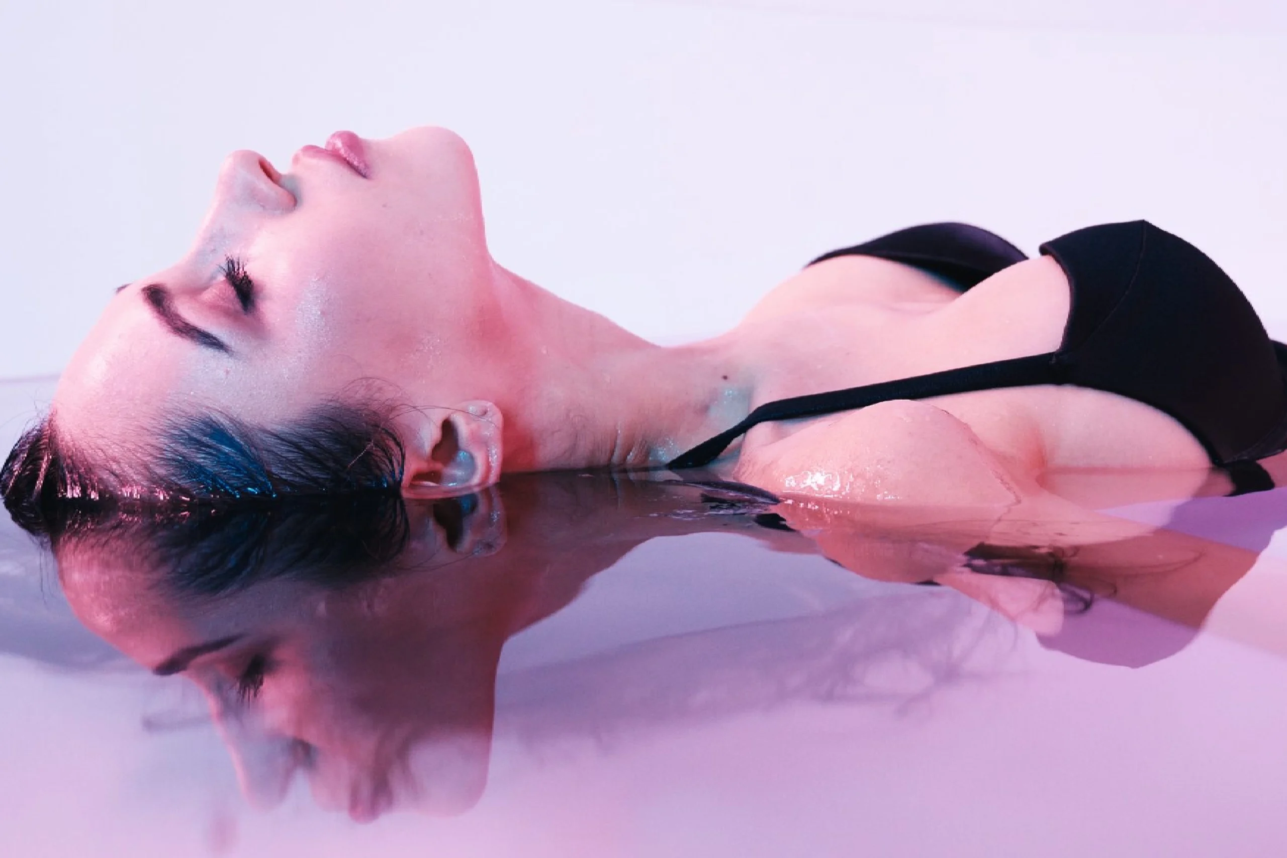 Person submerged in water with serene expression and reflection visible.